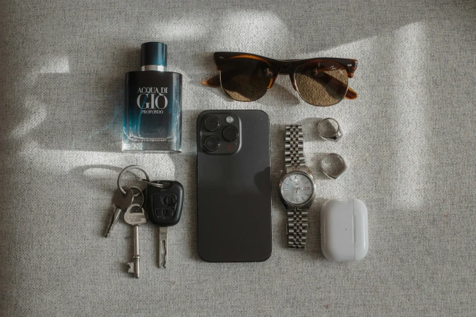 Perfume, sunglasses, phone, watch, keys, and earbuds arranged neatly arranged.
